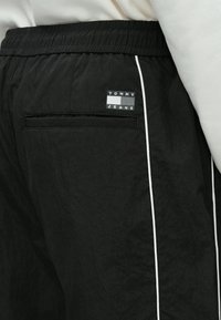 Μαύρο αθλητικό παντελόνι με υφή, με λευκή κάθετη ρίγα στο πλάι και μικρό κολαριστό λογότυπο Tommy Jeans στην πίσω τσέπη.