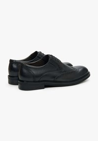 Czarne skórzane buty wizytowe z detalami w stylu brogue, gładkie wykończenie i okrągły czubek. Posiadają niski obcas i sznurowaną konstrukcję.
