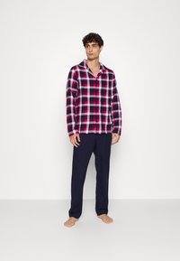 Karierte Flanell-Pyjama-Oberteile in Pink, Schwarz und Weiß, mit Kragen und Knöpfen, kombiniert mit marineblauen Hosen. Weicher Stoff, lockere Passform.