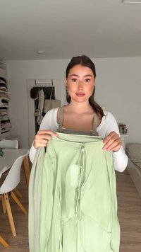 Indumento in tessuto leggero di colore verde chiaro, con dettaglio a coulisse, caratterizzato da maniche lunghe e design aperto, sorretto da una persona.