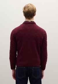 Maglione bordeaux lavorato a maglia con maniche a trecce testurizzate, collo e orlo a coste, abbinato a jeans blu scuro.