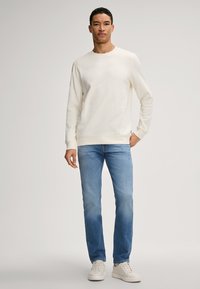 Jasna kremowa bluza z okrągłym dekoltem, zestawiona ze średnioblues dżinsami. Stylizację dopełniają białe buty sznurowane.