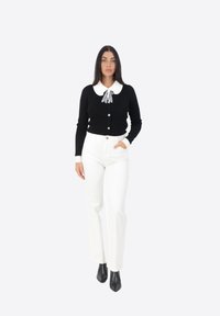 Cardigan nero con colletto bianco e fiocco, dotato di bottoni. Abbinato a pantaloni bianchi a vita alta e stivaletti neri con tacco.