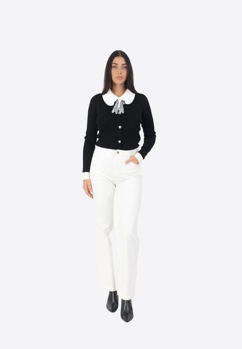 Cardigan nero con colletto bianco e fiocco, dotato di bottoni. Abbinato a pantaloni bianchi a vita alta e stivaletti neri con tacco.