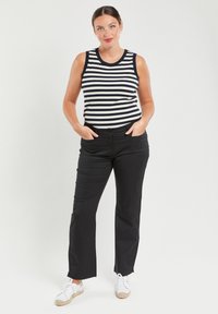 Pantalones negros y una camiseta sin mangas a rayas azul marino y blanca. El conjunto presenta una textura suave, un diseño ajustado y un estilo clásico, complementado con zapatos blancos.