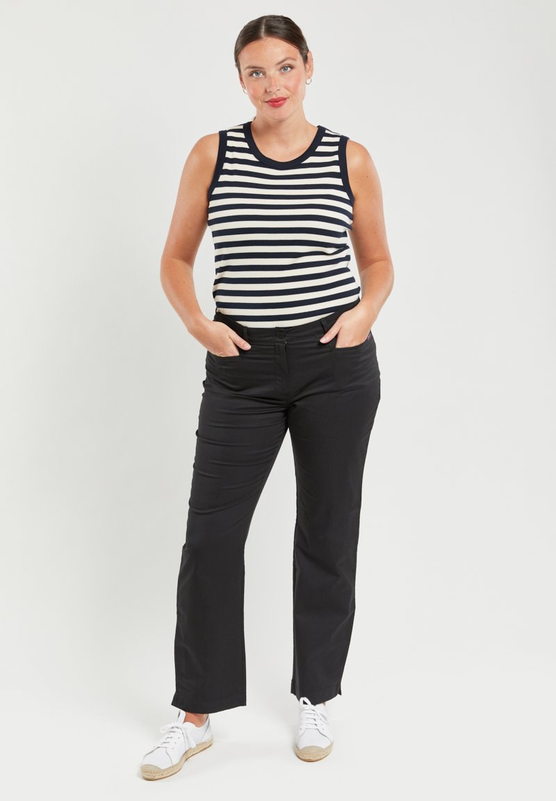 Pantalones negros y una camiseta sin mangas a rayas azul marino y blanca. El conjunto presenta una textura suave, un diseño ajustado y un estilo clásico, complementado con zapatos blancos.