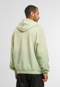 Sweat à capuche vert clair avec une coupe décontractée, doté d'un cordon de serrage et de poignets côtelés. Texture douce avec une finition légèrement délavée.