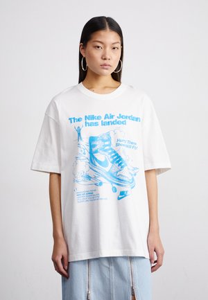 T-shirt blanc surdimensionné en coton, avec un design graphique bleu représentant une basket et un texte sur Nike Air Jordan, avec des manches courtes.