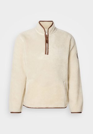 Kreemivärvi fliispullover neljanda tõmbluku jaoks; kaeluse ja varrukate ääred on pruunid. Pehme tekstuur, mugav lõige ja küljetaskud.