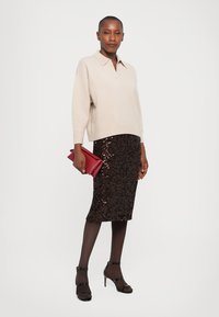Beige knitted sweater with a collar, paired with a brown sequin pencil skirt. Accessorized with a red clutch and black strappy heels.