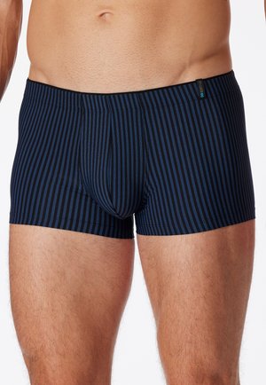 Man wearing dark blue boxer briefs with thin vertical black stripes, showing midsection and upper thighs against a white background.