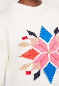 Weißer Strickpullover mit einem bunten geometrischen Muster in Pink, Rot, Blau, Schwarz und Beige. Klassisches Rundhalsausschnitt-Design.