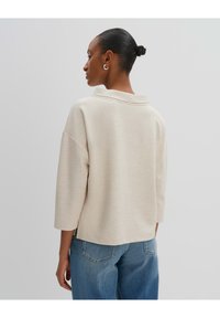 Felpa oversize color crema con colletto a falda, maniche 3/4 e tessuto texture, abbinata a jeans azzurri chiari.
