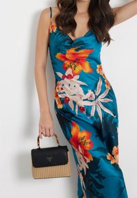 Robe fleurie avec des fleurs orange et blanches éclatantes sur un fond turquoise, associée à un sac à main noir tressé avec une poignée en bambou.