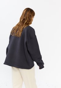Overmaat grijze sweatshirt met verlaagde schouders en geribbelde manchetten. G gedragen met lichte broeken met een relaxte pasvorm.