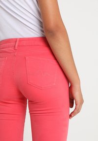 Růžové džíny ze směsového denimu s úzkým střihem, zadními kapsami a jemným vlnitým prošíváním. Tkanina vypadá hladce s mírným leskem.