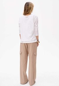 Weißes Langarmoberteil mit lockerer Passform, kombiniert mit beigen, weit geschnittenen Cargo-Hosen, die seitliche Taschen und eine glatte Textur aufweisen.
