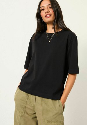 Black short-sleeve top with a relaxed fit, made from soft cotton. Features a crew neckline and hangs loosely over beige cargo pants.