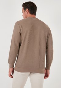 Felpa marrone a coste con maniche lunghe e scollatura rotonda, caratterizzata da una texture uniforme e una vestibilità comoda, vista da dietro.