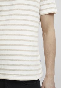 Stripete t-skjorte i krem og beige, korte ermer, laget av en bomullsblanding, med rett nederkant og et lite merke på siden.