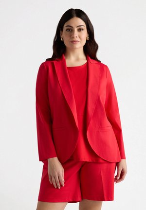 Blazer rosso con un design su misura, caratterizzato da un bavero a sacchetto e due tasche frontali, abbinato a un top e pantaloni corti rossi coordinati.