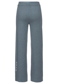Grijze wijde broek van zacht materiaal. Beschikt over een elastische tailleband en het woord "SAND" in lichtgrijs gedrukt op het linkerpantalon.