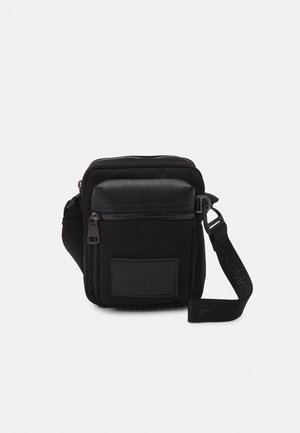Compact black crossbody bag with multiple zippered compartments, one with a leather flap, and an adjustable strap with Calvin Klein branding.