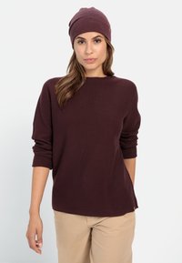 Bordeauxfarbenes Strickpullover mit rundem Ausschnitt und umgeschlagenen Bündchen, kombiniert mit einer passenden Mütze. Weiche Textur und lockere Passform.