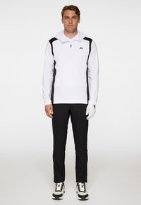 Vit tröja med svarta sidopaneler, kvart zip och huva. Kombinerad med svarta byxor och vita/glansiga svarta sneakers, samt en vit handske.