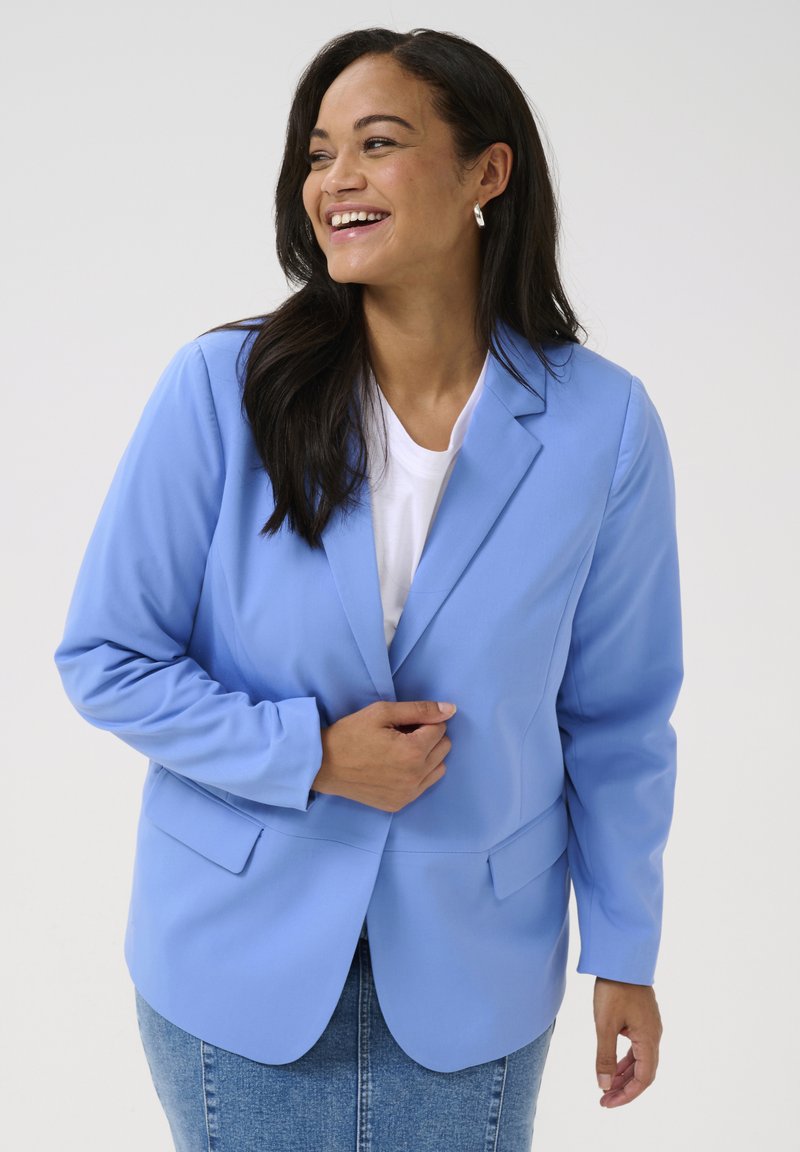 Blazer azul claro, diseño de un solo boton, dos bolsillos frontales, tela texturizada, combinado con una camisa blanca y una falda de mezclilla.