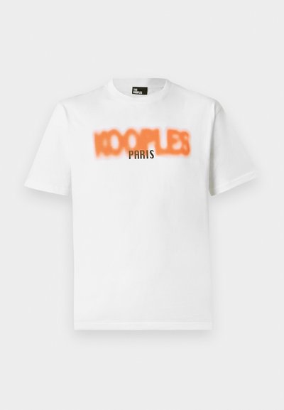 White cotton t-shirt featuring blurred orange text "KOOPLES" and clear black text "PARIS" on the front. Short sleeves, crew neck design.
