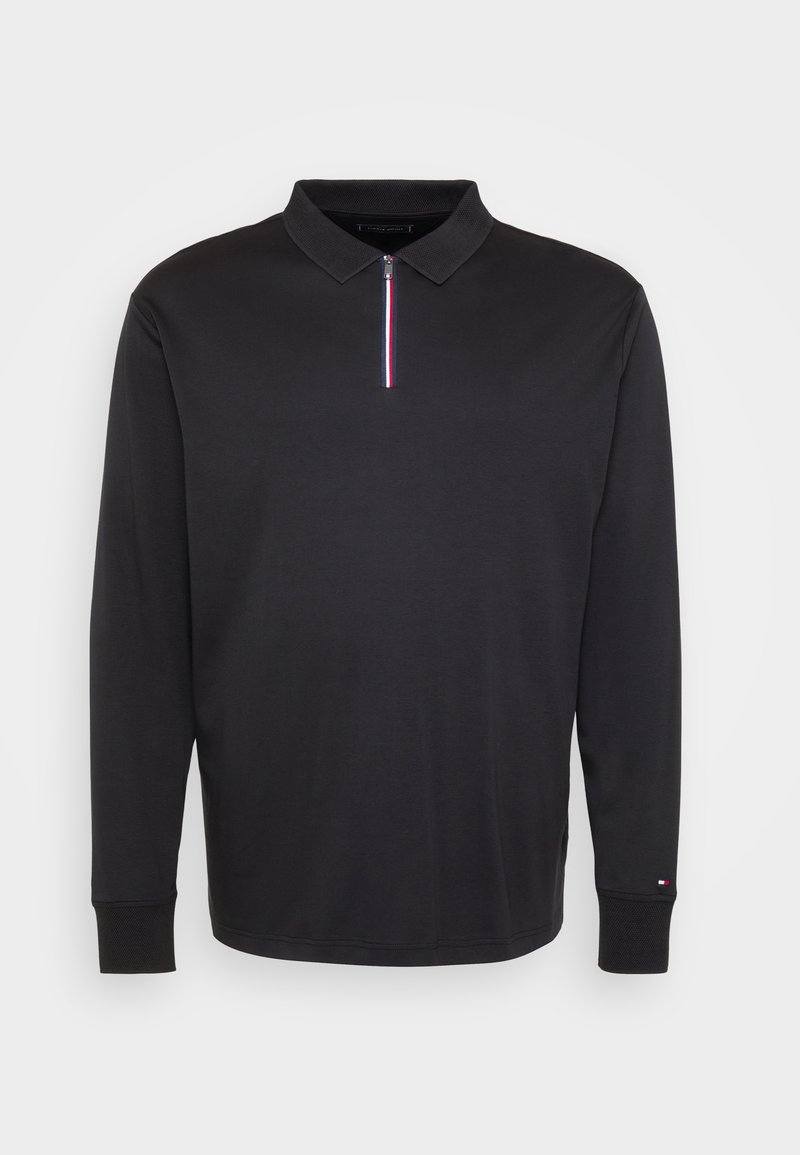 Schwarzes Langarm-Polohemd mit geripptem Kragen, Reißverschluss vorne mit roter, weißer und blauer Linie und kleinem Logo am linken Bündchen.