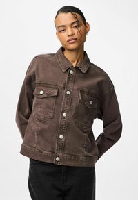 Brun denimjakke med krave, to frontlommer og sølvknapper, med en afslappet pasform og synlige syninger.