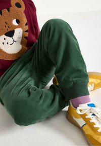 Gröna kordfläskbyxor med ribbade avslut, tillsammans med gula sneakers med vita och blå accenter samt ljuslila strumpor.