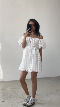 Vestido branco de ombros à mostra com mangas bufantes, cintura elástica e padrão quadriculado. Usado com ténis cinzentos e brancos.