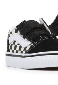 Chaussures pour tout-petits en damier noir et blanc avec des bandes Velcro, en matériau suédé, semelle en caoutchouc et coutures blanches contrastantes.
