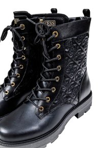 Bottes en cuir noir à lacets avec des côtés à motif matelassé, œillets dorés, semelles épaisses et étiquettes de logo Guess sur la languette.