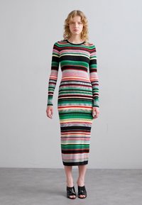 Abito a maniche lunghe a righe con colori multipli: nero, verde, rosso e rosa. Design aderente con lunghezza fino al polpaccio. Indossato con tacchi neri aperti.