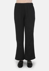 Black, wide-leg pants with an elastic waistband. Made of a soft, textured fabric. The hemline is slightly flared. Paired with black loafers.