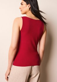 Top sin mangas rojo de tejido suave, con escote redondeado y forma ajustada. Combinado con pantalones beige texturizados.
