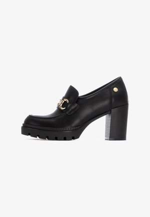 Mocasines de cuero negro con tacón bloque grueso, que presentan herrajes en tono dorado y una suela texturizada para mayor agarre y estabilidad.