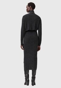 Tummanharmaa neulottu mekko, jossa on lyhyt selkäosa, pitkät hihat ja ribbineulos. Mekossa on sivuhalkiot ja se on yhdistetty polven korkeisiin mustiin saappaisiin.