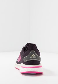 Fialová sportovní bota s růžovými akcenty, texturovaný pletený svršek, polstrovaná bílá podešev a stříbrné logo Adidas na patě.