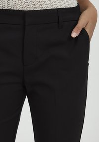 Black tailored pants with a smooth texture, featuring side pockets and a sleek design. The waistband is flat with a subtle crease down the front.