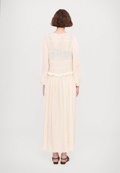 Long, cream-colored dress made of lightweight, crinkled fabric with a fitted bodice, ruffled hem, and button closure at the back.