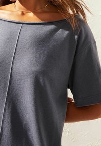 Chemise grise à manches courtes avec un décolleté dénudé. Tissu doux au toucher. Présente un détail de couture centrale pour une touche de design.