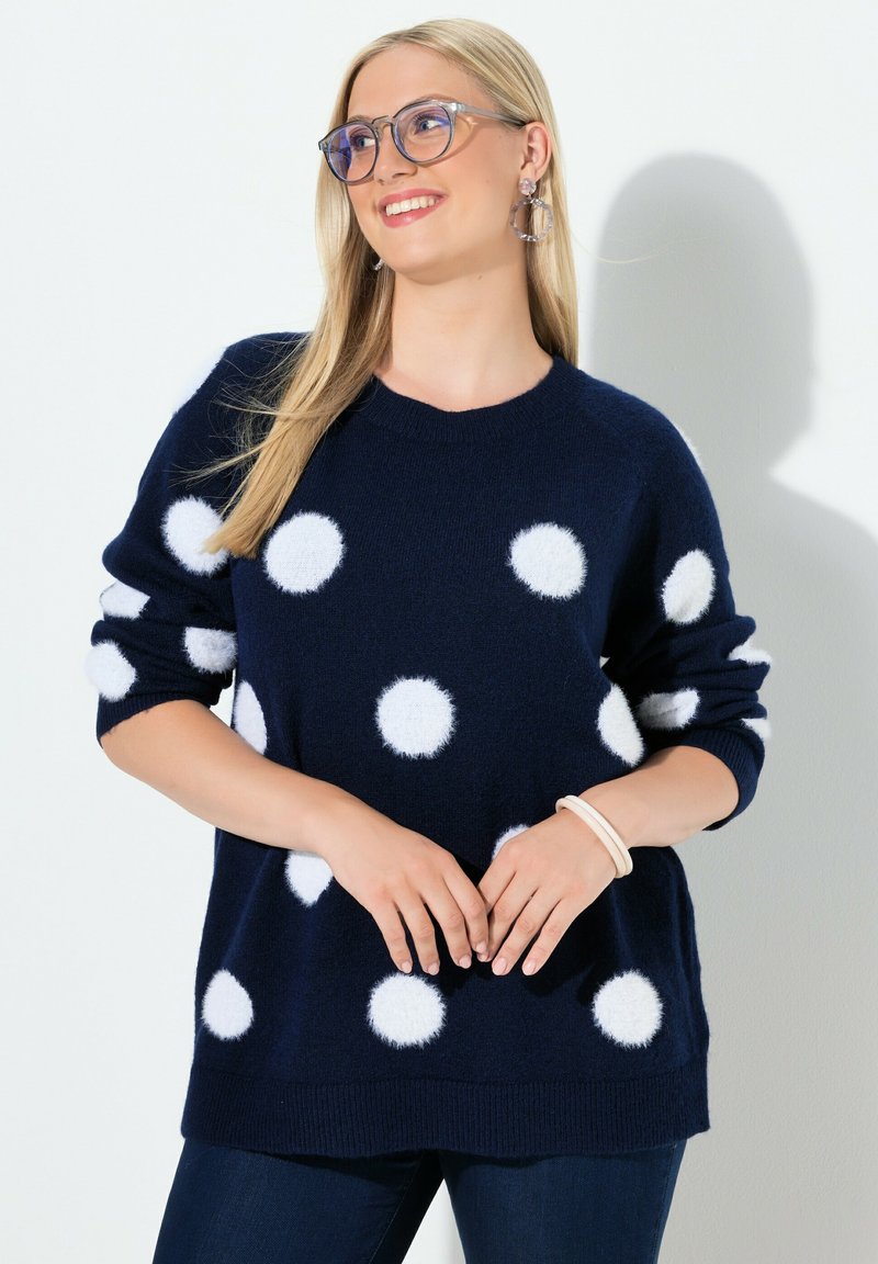 Námořnický modrý svetr s velkými bílými puntíky, vyrobený z měkkého materiálu. Má kulatý výstřih a žebrované manžety.