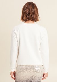 Weißes Sweatshirt mit einem gerippten Rundhalsausschnitt und Raglanärmeln. Weiches Material mit einer glatten Textur. Kombiniert mit einem pailettenbesetzten Rock.