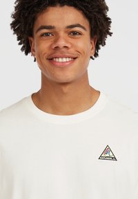 T-shirt in cotone bianco con scollo rotondo, caratterizzato da un piccolo logo O'Neill triangolare sul lato sinistro del petto in colori blu, rosa e giallo.
