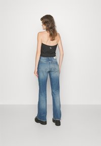 Top nero senza spalline, jeans blu a zampa d'elefante con leggera variazione di lavaggio e stivali neri chunky. Design semplice senza motivi visibili o accessori.